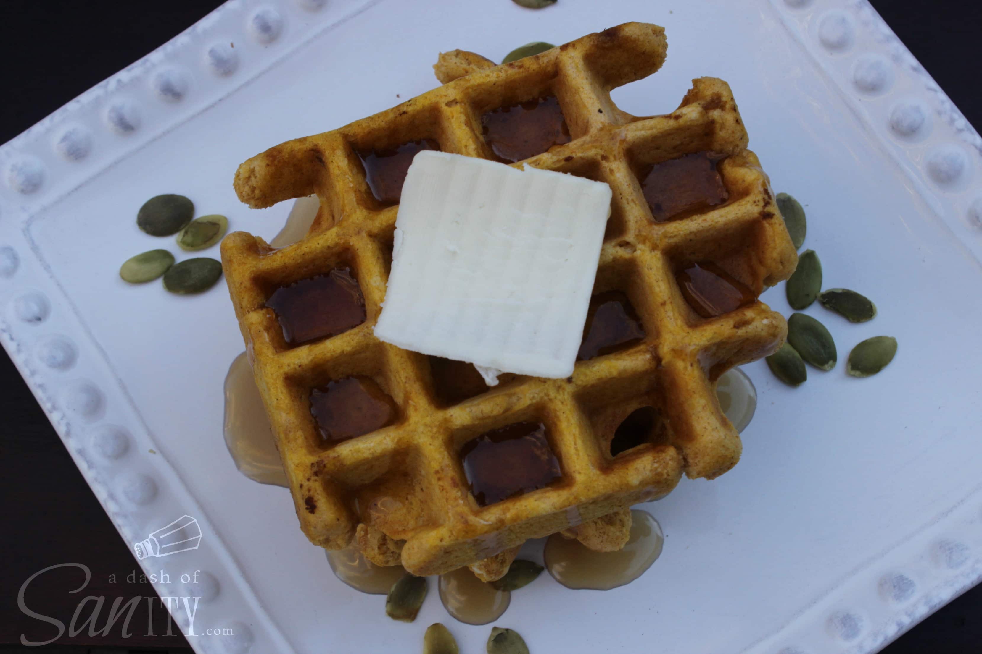 overhead Pumpkin Waffles served on a plate with a pat of butter, syrup, and pepita seeds