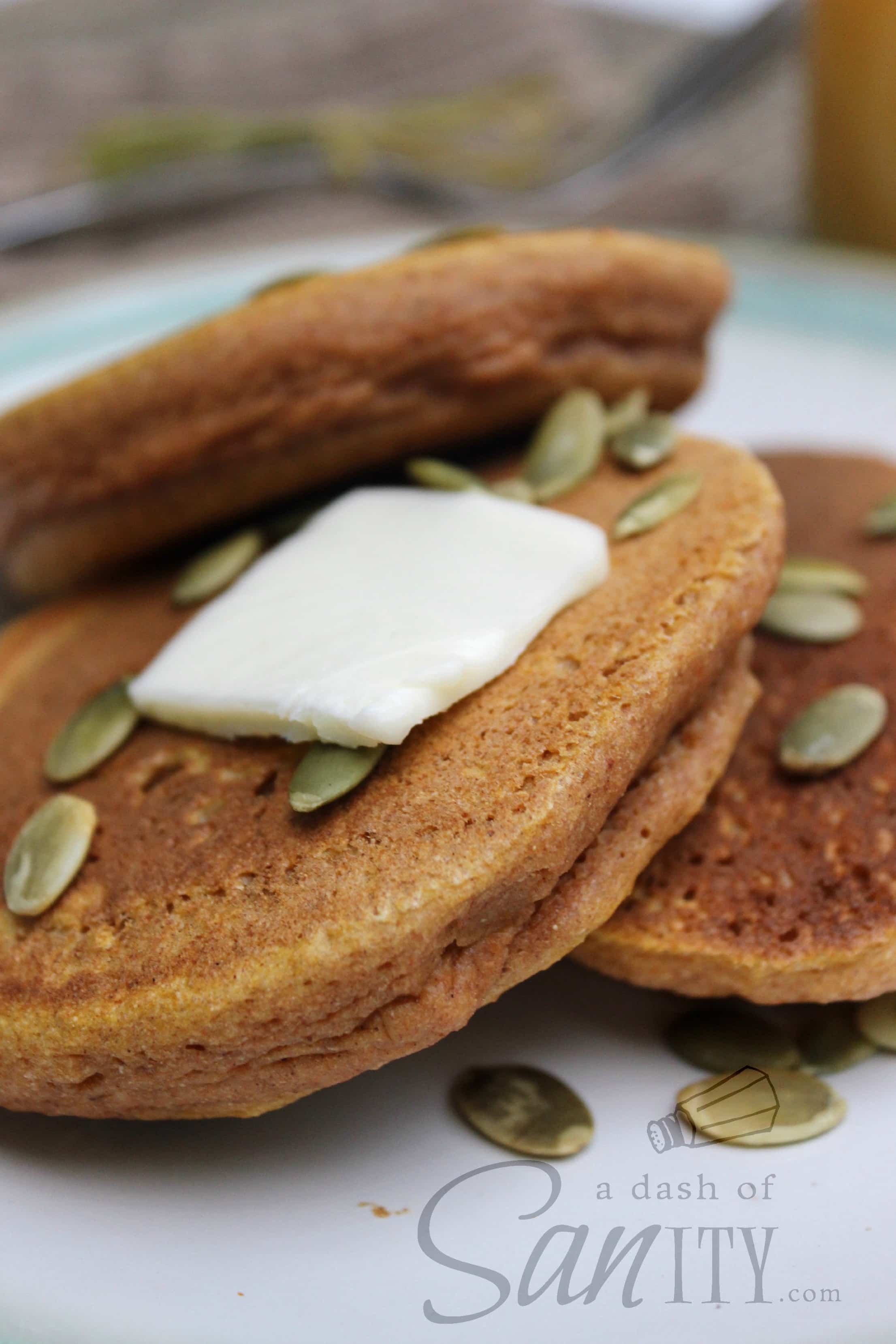Whole Wheat Pumpkin Pancakes served on a plate with pepitas and a pat of butter on a plate