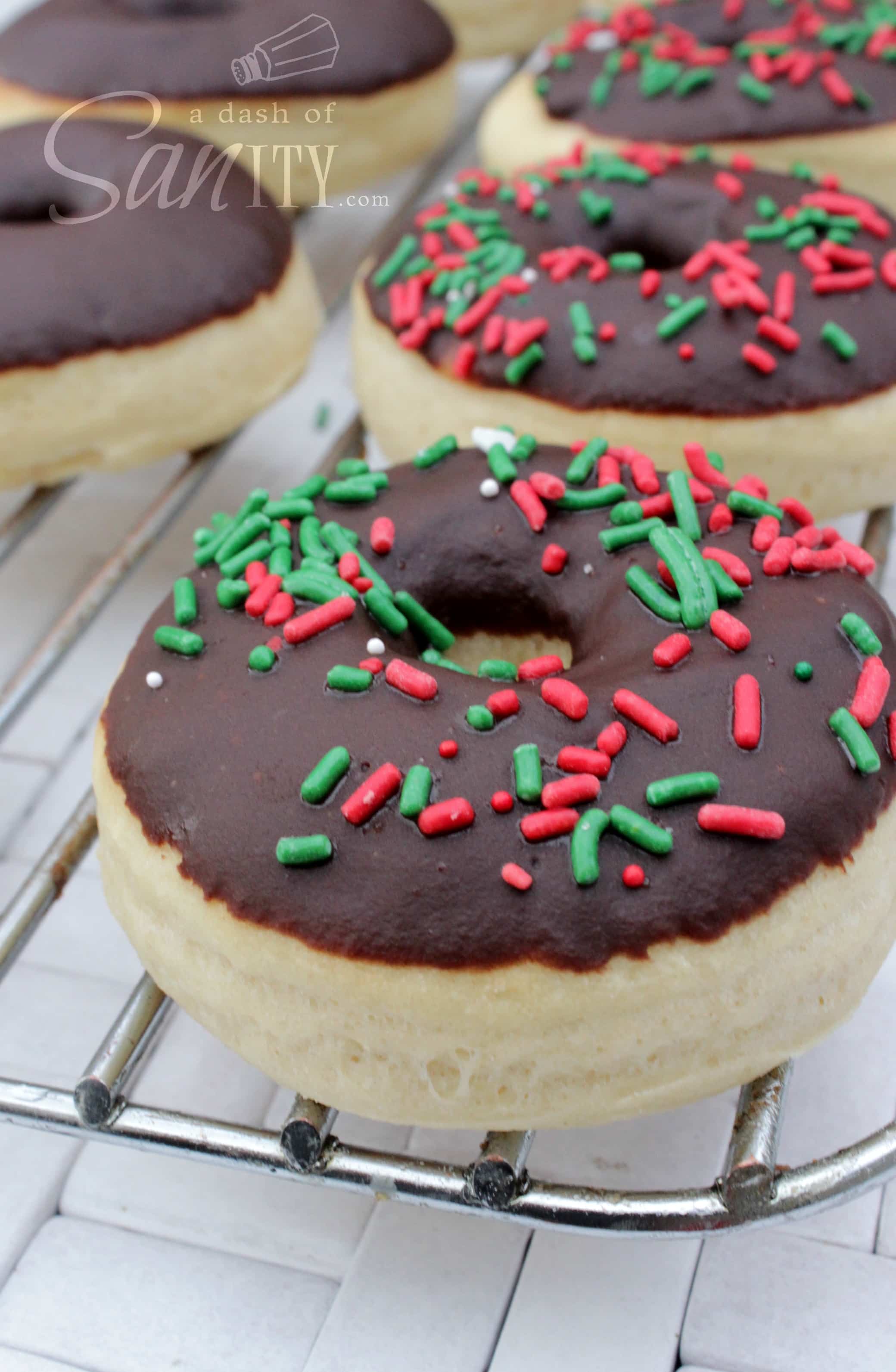 Baked Chocolate Glazed Doughnuts with red and green sprinkles on a metal cooking rack