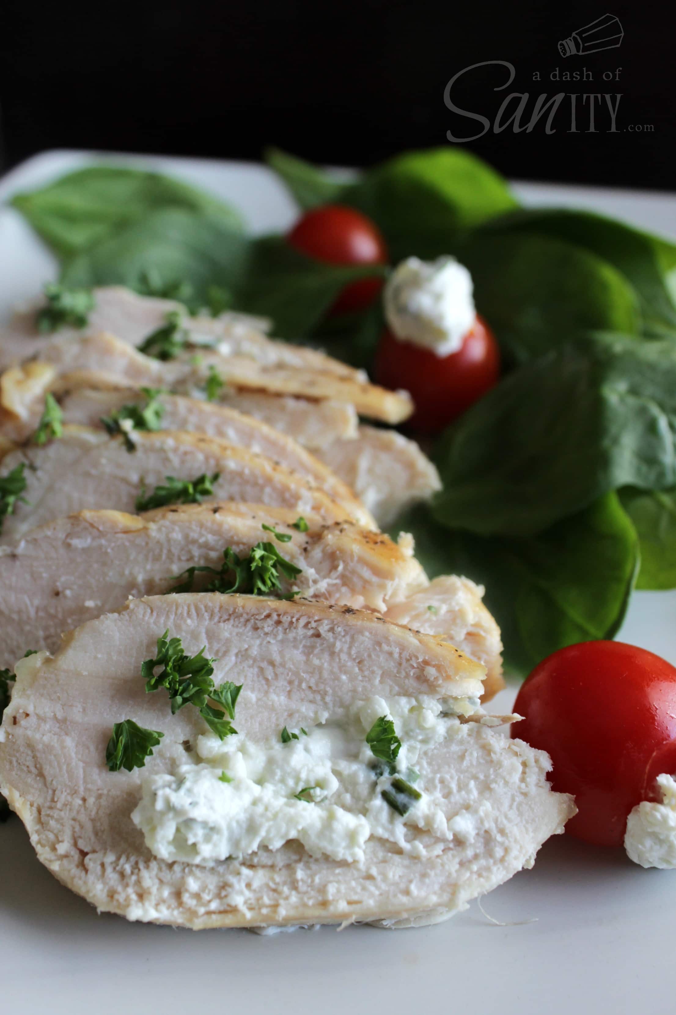 Chive & Garlic Stuffed Chicken Breast sliced and served on a plate with fresh spinach and tomoatoes