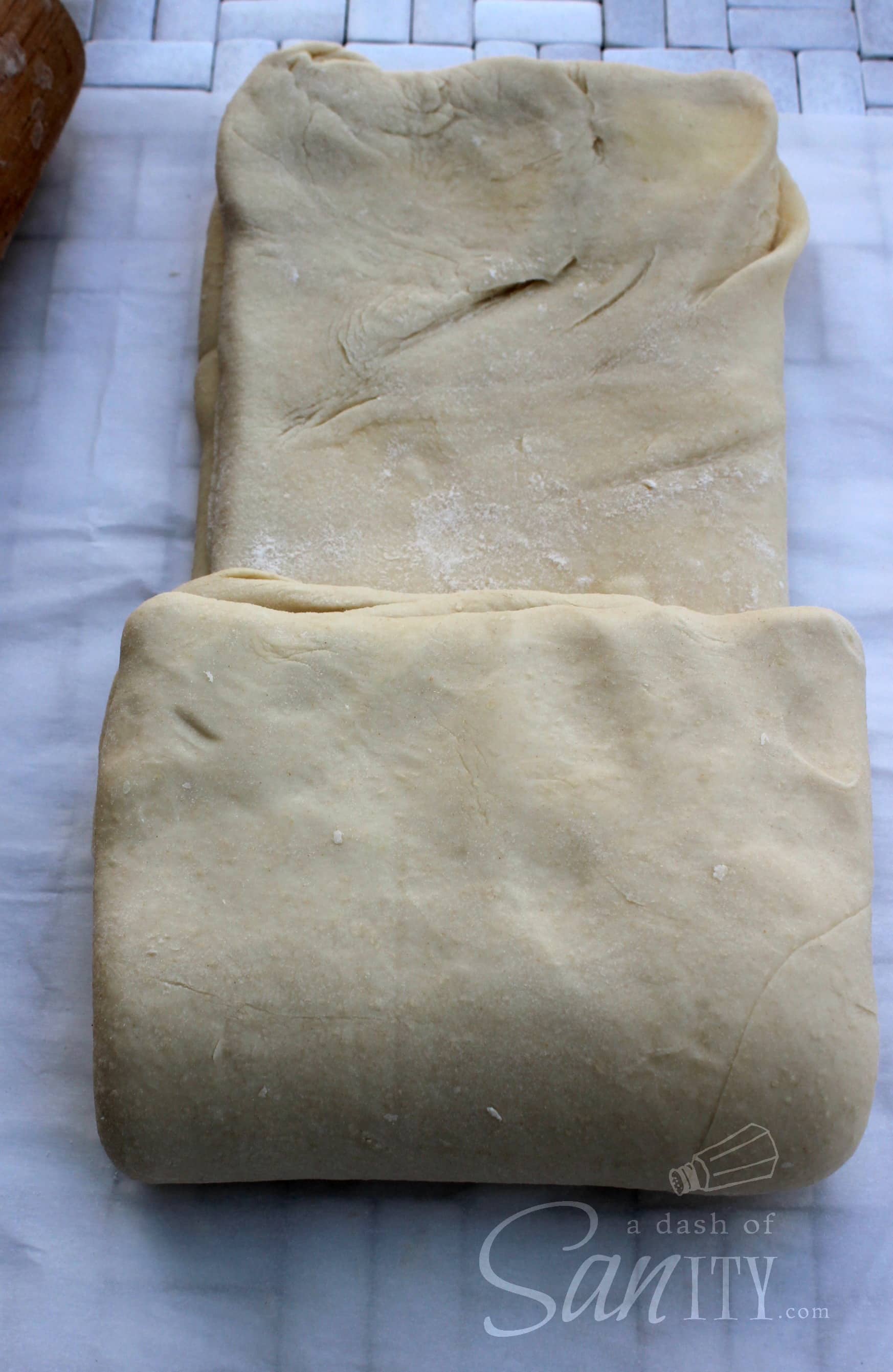 These Chocolate Croissants are light, flaky, buttery croissants with a deliciously rich dark chocolate center. A perfect treat for any chocolate lover. croissant dough being folded back into a square