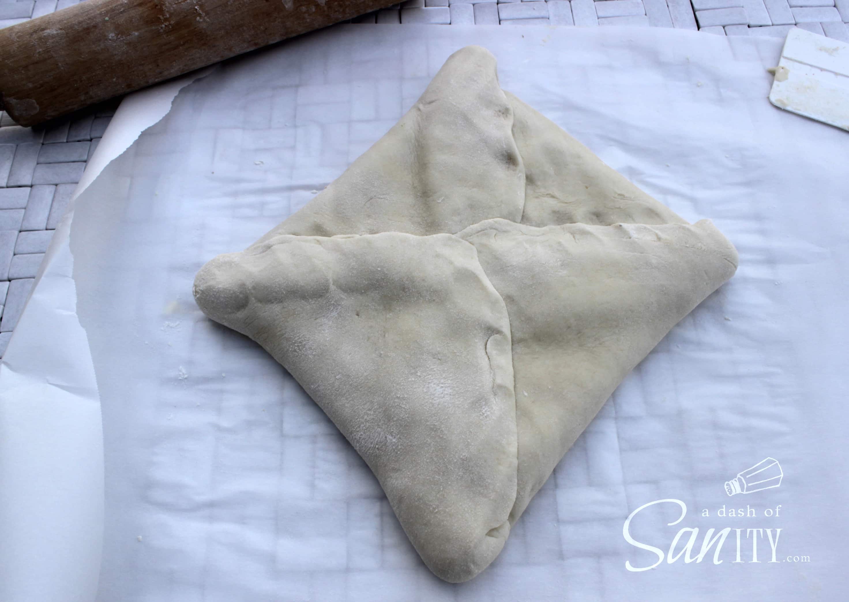 These Chocolate Croissants are light, flaky, buttery croissants with a deliciously rich dark chocolate center. A perfect treat for any chocolate lover. croissant dough on parchment folded around the butter square with seams pressed together