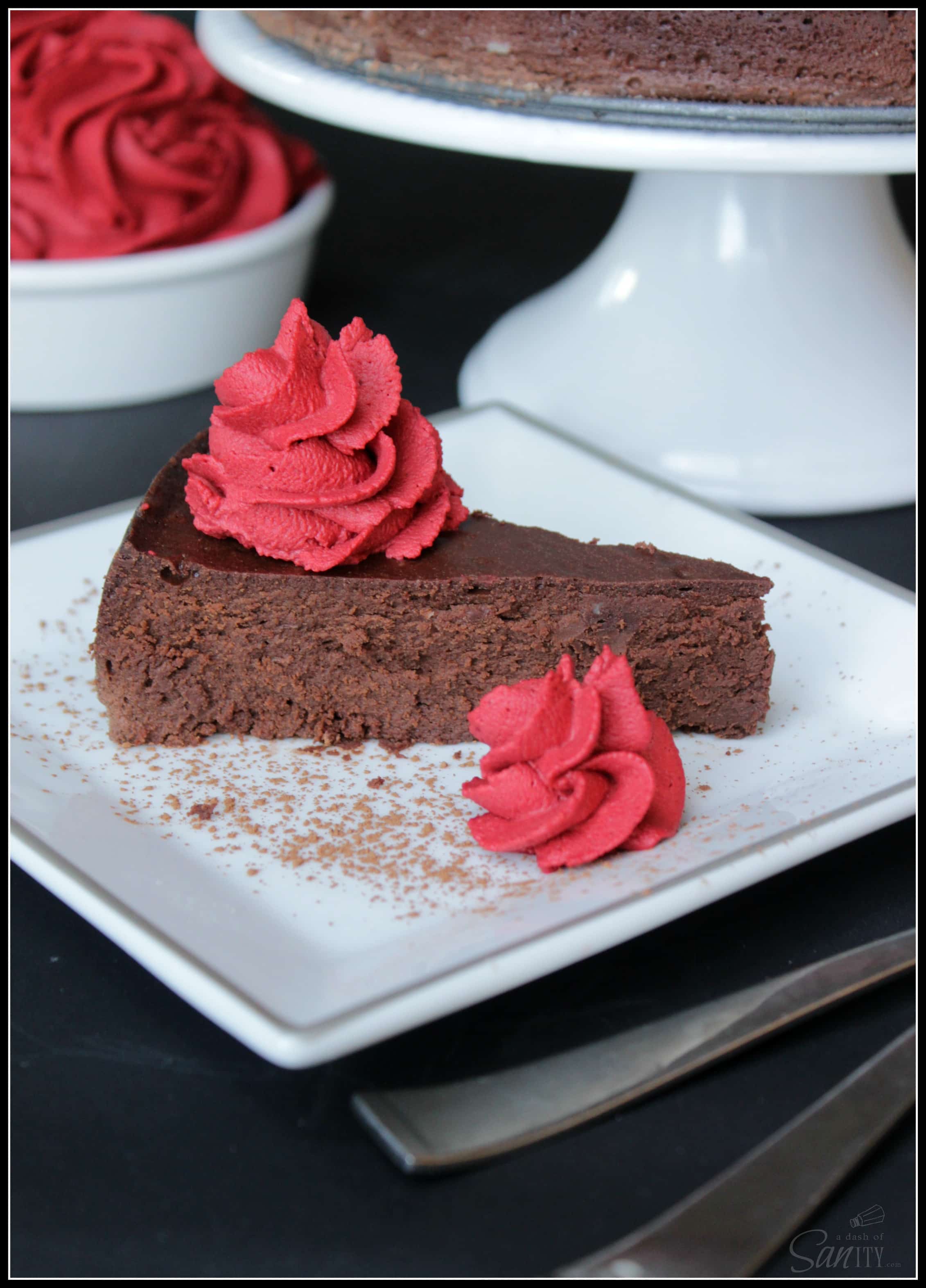 Decadent Chocolate Flourless Cake with Red Velvet Mousse slice on a small plate with cake on a stand in background