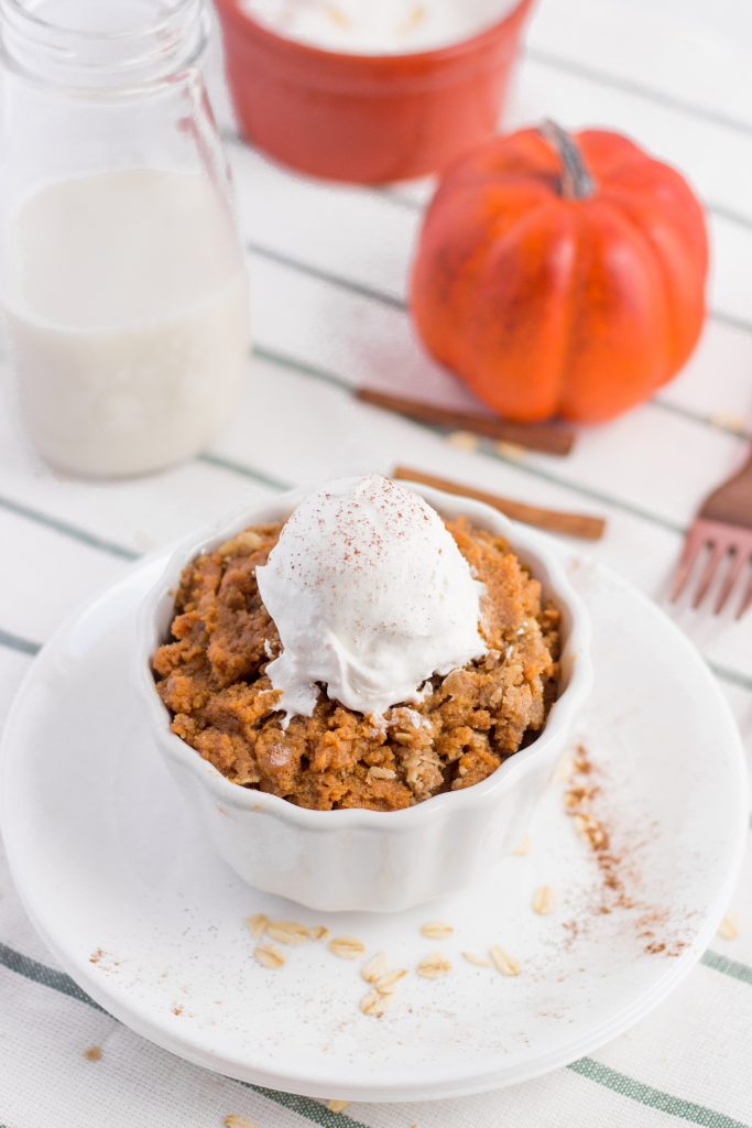 Pumpkin Crisp Pie in a small white serving bowl topped with whipped cream, next to a glass of milk