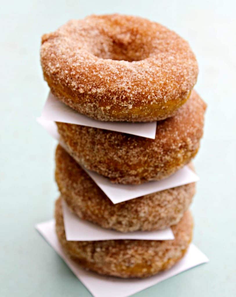 photo of 4 cinnamon sugar pumpkin donuts stacked with parchment paper between each