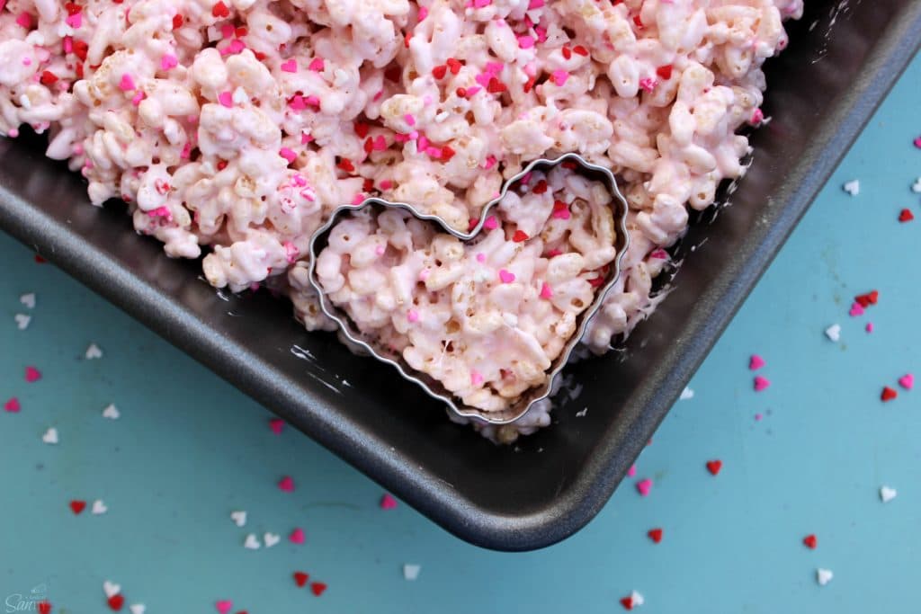 Show someone how much you love with these ooey, chewy & delicious VALENTINE'S RICE KRISPIE TREATS. Easy, delicious and irresistible Valentine’s Day Rice Krispies Treats in a metal baking pan with a heart shaped cutter in corner of treat