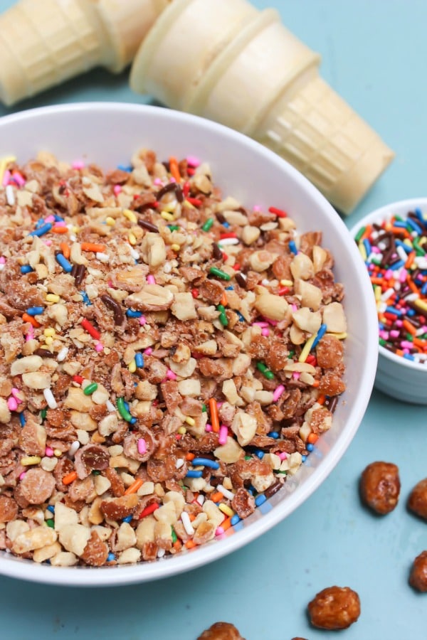 Copycat Dairy Queen Crunch Cone aka "Crunch Coat" recipe is the best ice cream topping you will ever have! Time to move over hot fudge. photo of crunch cone topping in a white bowl, with cones and sprinkles in background
