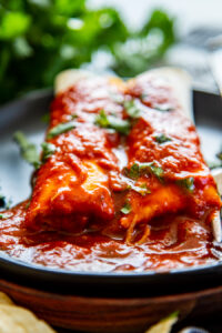black plate with 2 cheese enchiladas with red sauce