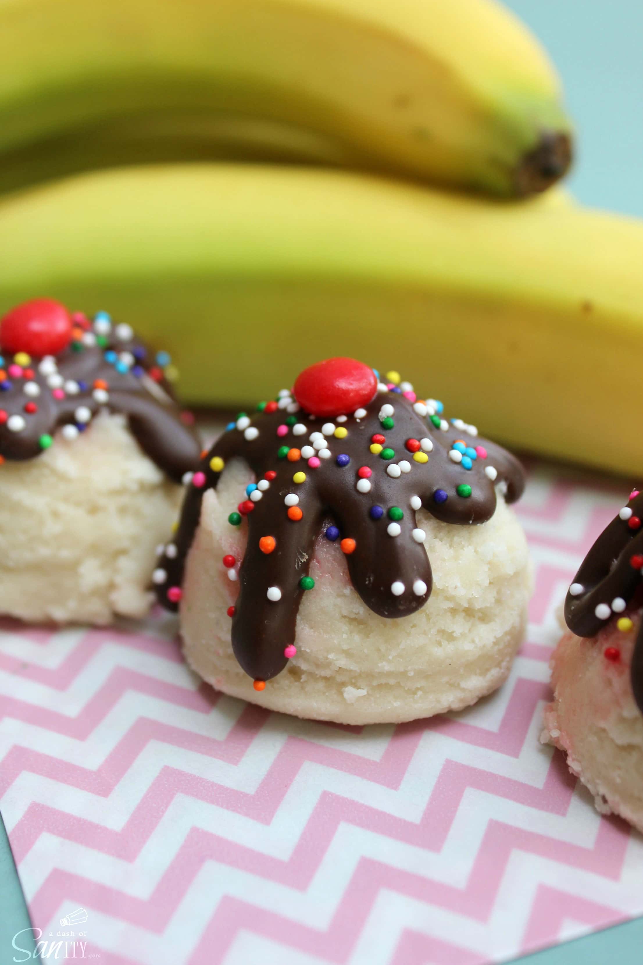 Banana Split Cookie Dough Bites are little bites of an ice-cream classic. Banana sugar cookie dough with a cherry center, topped with chocolate & sprinkles. Banana Split Cookie Dough Bites on plate