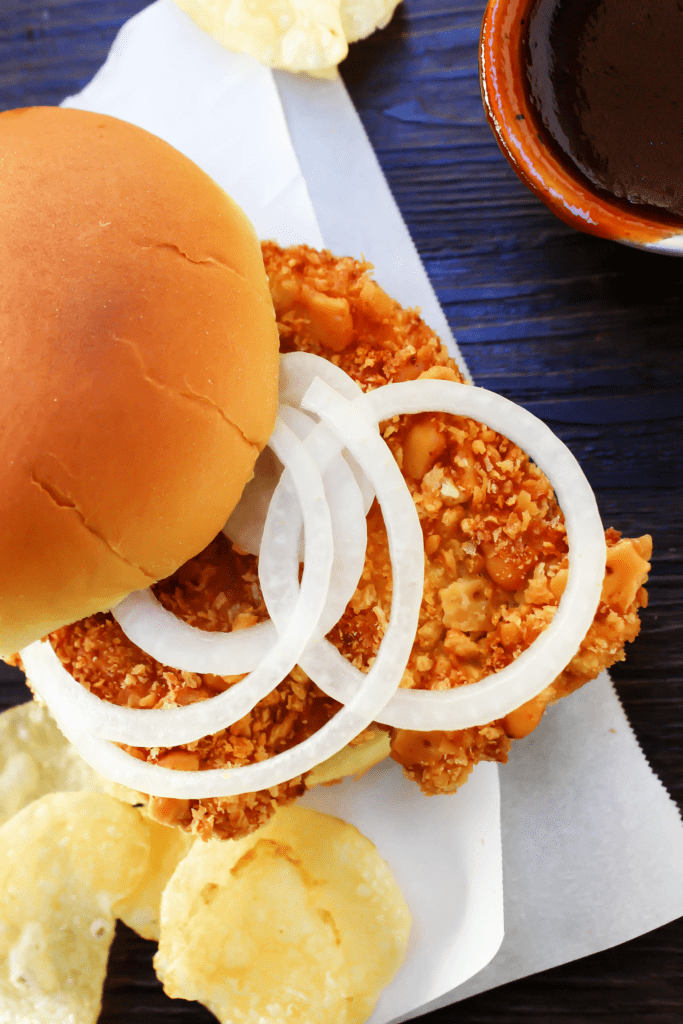 Crispy Pork Tenderloin Sandwiches deliciously crispy on the outside, tender and juicy in the center, these Iowa-inspired sandwiches will become a favorite. overhead Pork Tenderloin Sandwich on parchment, with top bun moved to the side showing onion slices on top of crispy pork, potato chips and BBQ sauce on the side