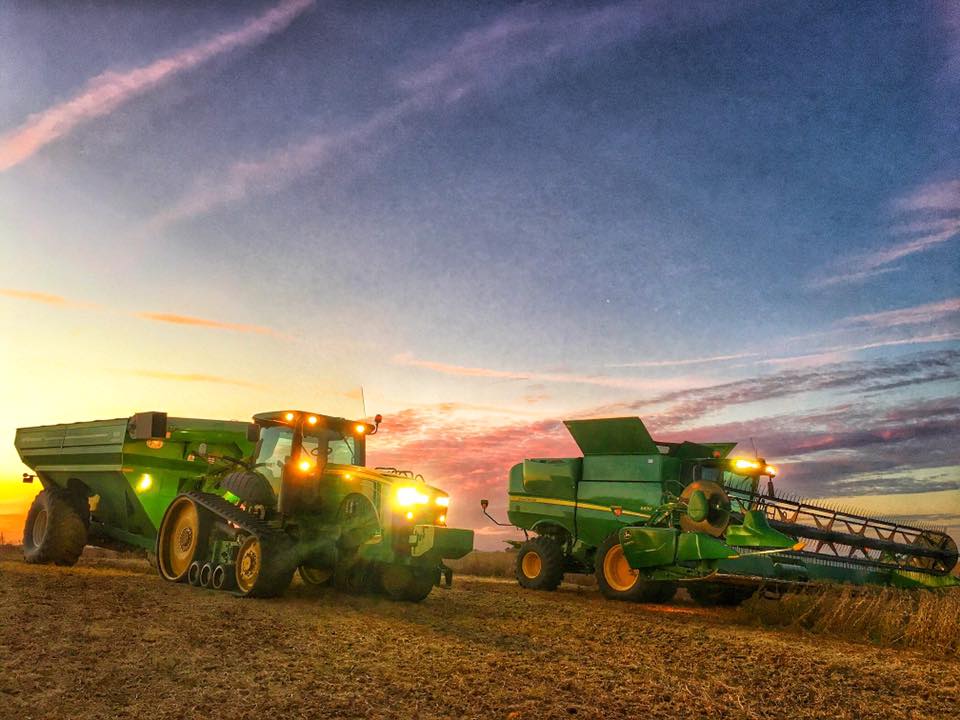 two different tractors with headlights on harvesting a field at night