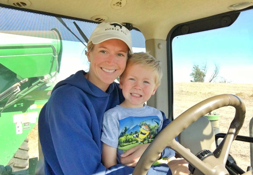 a woman with a young boy on her lap sitting in the driver seat of a tractor