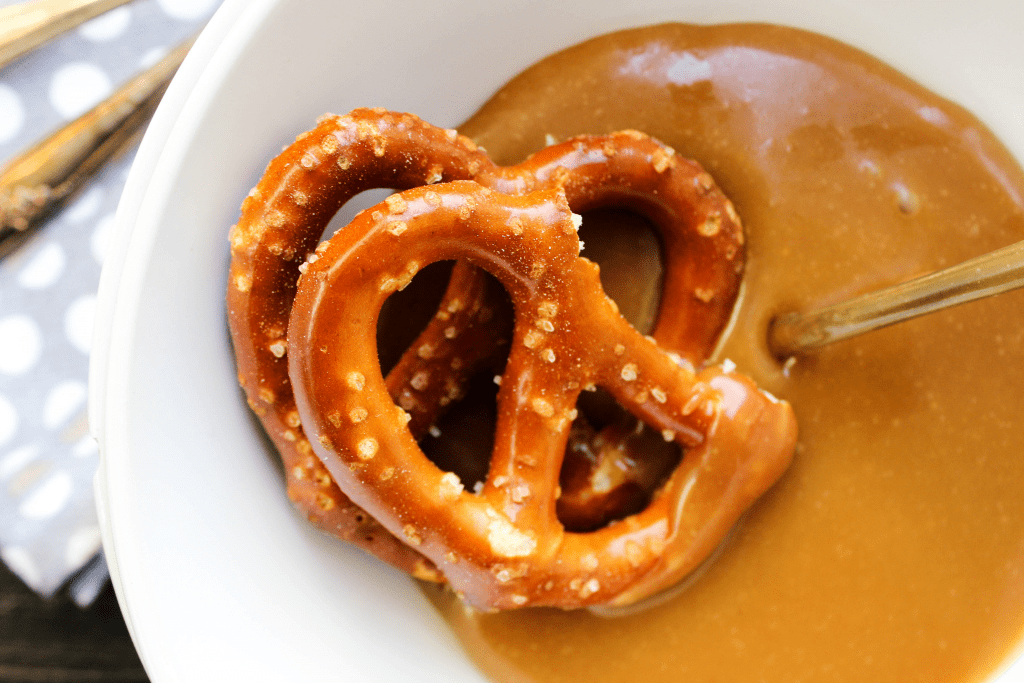 Friends, you’re only ten minutes from peanut butter and caramel euphoria. Ten minutes is all is takes to make this PEANUT BUTTER CARAMEL SAUCE! Peanut Butter Caramel Sauce in a bowl with 2 hard pretzels and a spoon