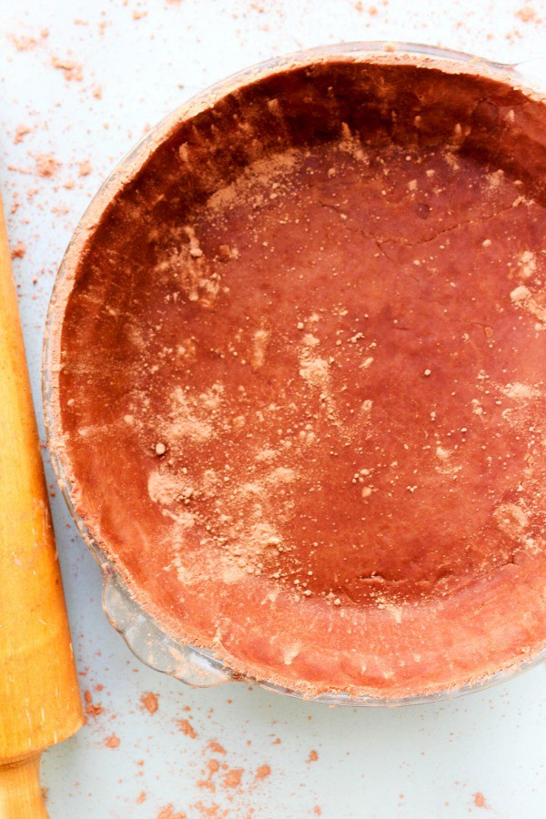 chocolate pie crust pressed into a glass pie pan next to a rolling pin
