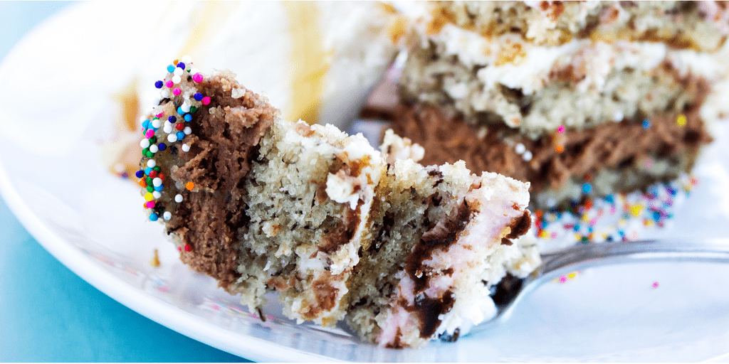 Banana Split Cake is a rich banana cake layered with chocolate, pineapple, and strawberry buttercream that is topped with ganache, cherries, and sprinkles.