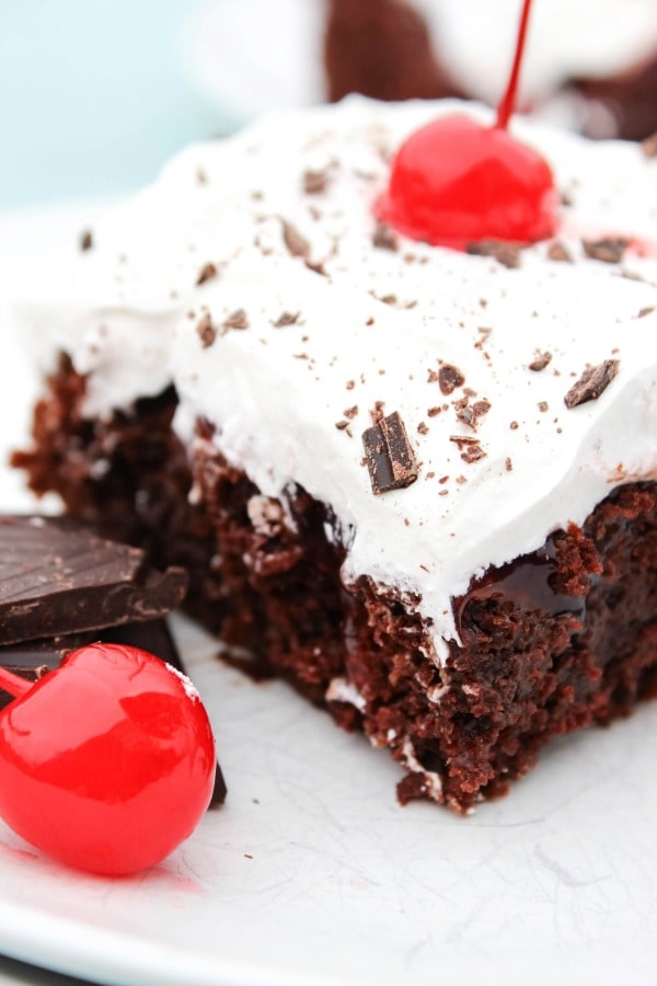 photo of a slice of Black Forest Poke Cake on a plate topped with maraschino cherries