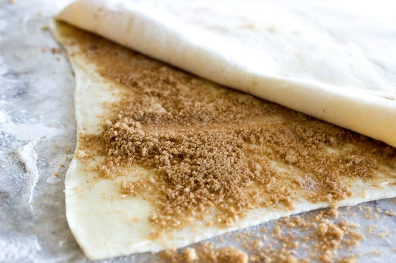photo showing how to assemble puff pasty, with bottom layer of pastry, then a layer of butter and cinnamon-sugar, then another puff pastry on top.