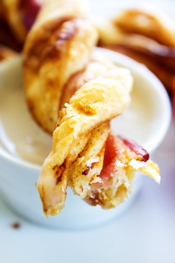 close up of Crispy Bacon Cinnamon Roll Twist, sitting over a small white bowl of icing
