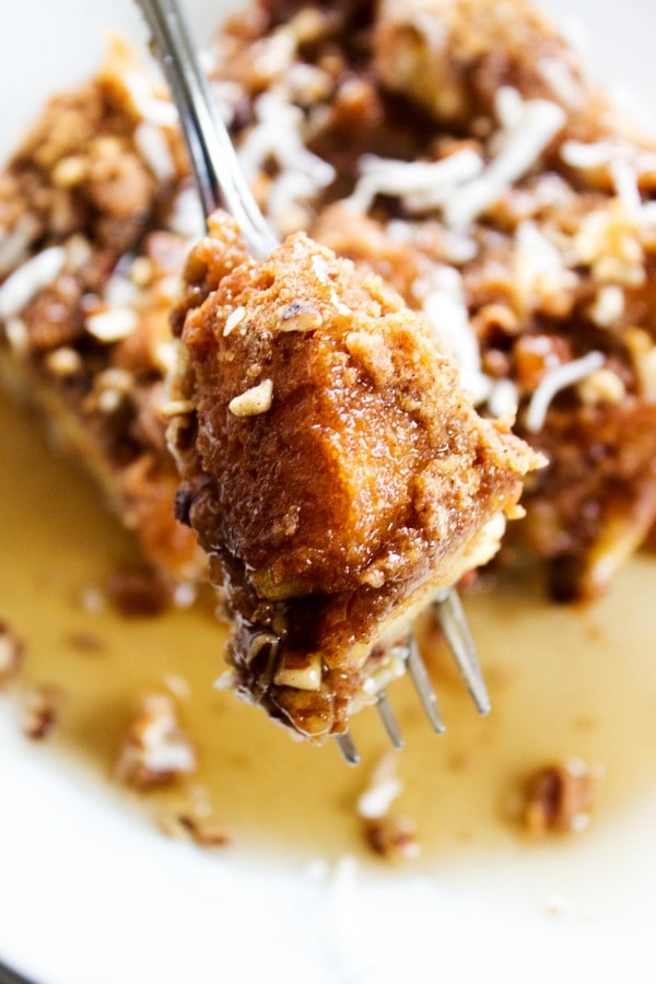 Overnight Coconut Cinnamon Pecan French Toast Casserole - Elevate your morning breakfast with this deliciously easy, make-ahead-breakfast casserole. photo of a bite of Overnight Coconut Cinnamon Pecan French Toast Casserole on a fork, above a plate with a slice of casserole on it