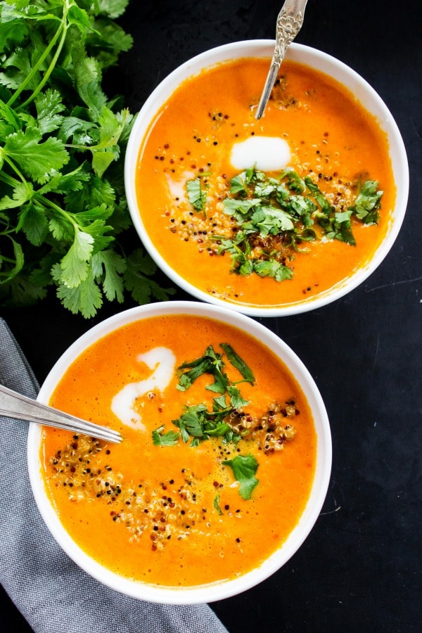 Thai Curry Red Pepper Quinoa Soup is an easy 30-minute meal made with red curry, coconut milk and quinoa. Skip take-out and make this healthy twist instead. top down photo of 2 bowls of Thai Curry Red Pepper Quinoa Soup with spoons, garnished with cream and cilantro