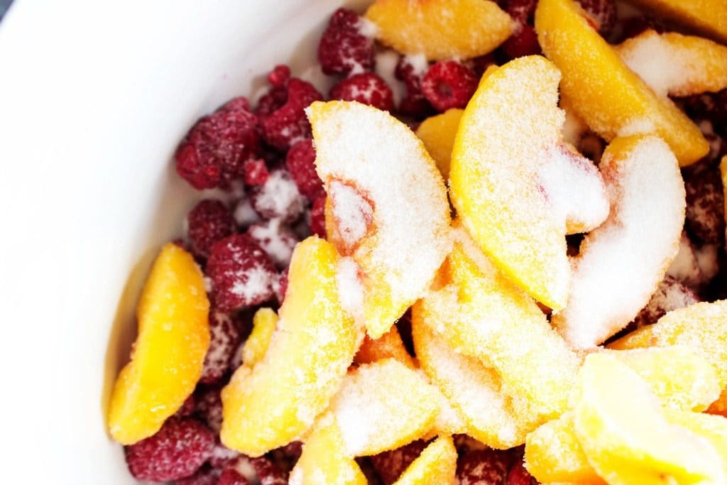 RASPBERRY PEACH SAUCE - a classic summer combination of peaches and raspberries made into a gorgeous sauce that will brighten any dish. From dessert to breakfast you will want to pour this sauce on it all. white bowl of frozen peaches and raspberries