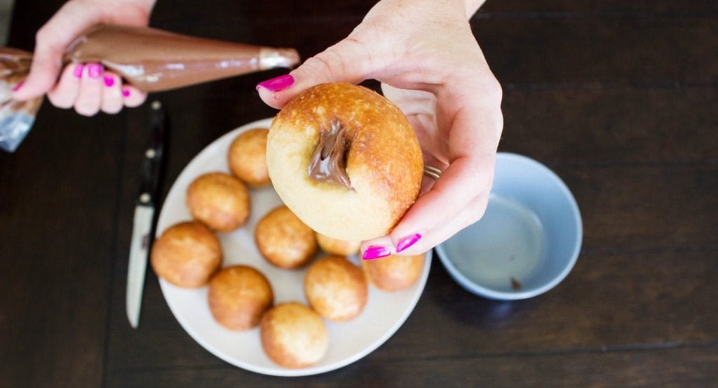 donut with hole it it being filled with Nutella