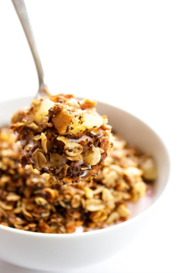 PINA COLADA GRANOLA - a tropical version of granola. Made with coconut, macadamia nuts and dried pineapple, this granola is a perfectly wholesome snack or breakfast. PINA COLADA GRANOLA - White bowl, white table, metal spoon