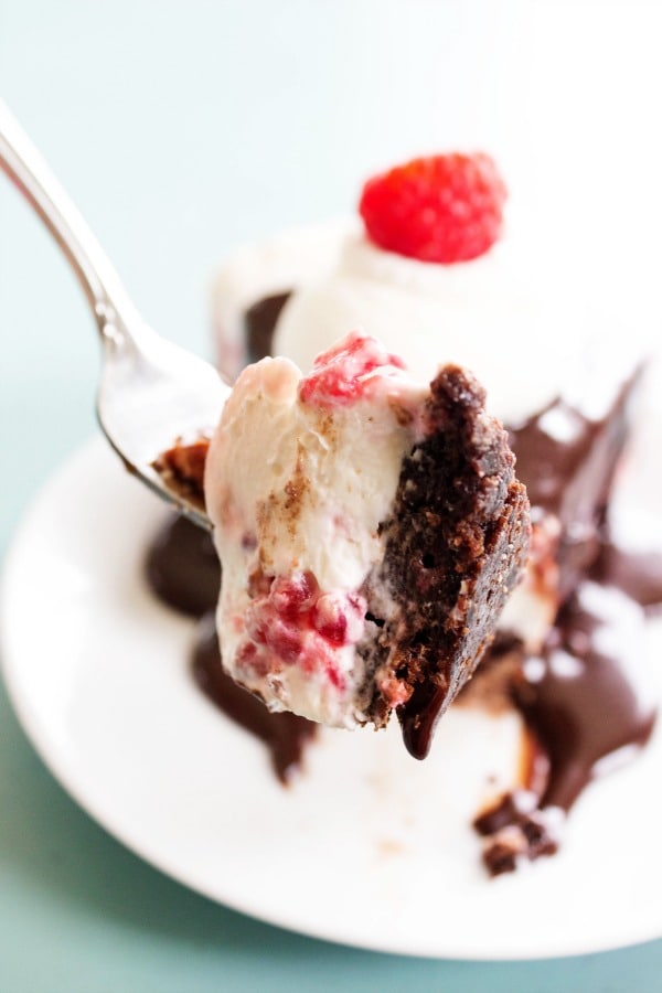 FUDGE BROWNIE NO BAKE RASPBERRY CHEESECAKE - the best ever hot fudge sauce drizzled over a fresh raspberry no bake cheesecake all on top of a fudgy delicious brownie. This is the dessert you have been craving. FUDGE BROWNIE NO BAKE RASPBERRY CHEESECAKE - Blue table, metal fork, white plate