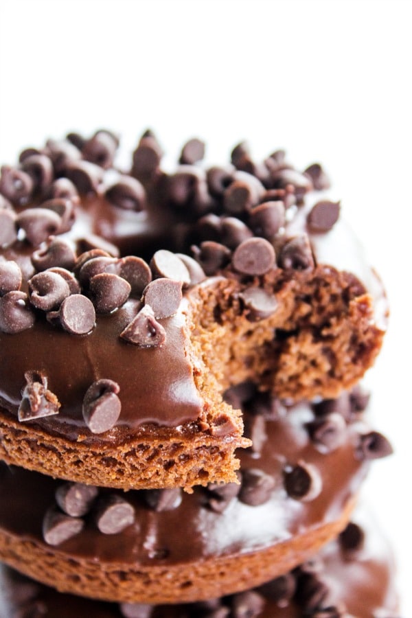Triple Chocolate Baked Cake Donuts - a Devil's Food Cake Donut, glazed with a chocolate ganache and topped off with mini-chocolate chips. TRIPLE CHOCOLATE BAKED CAKE DONUTs RECIPE - bite out of donut on white table