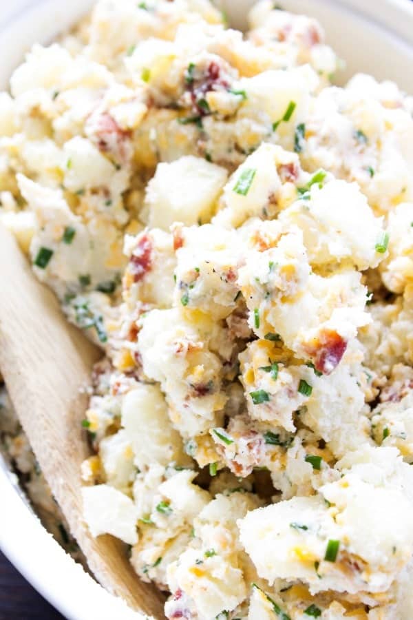 BEST EVER POTATO SALAD RECIPE - loaded with bacon, chives, cheese and ranch seasoning, this potato salad will become a traditional family barbecue recipe. potato salad bacon, chives, cheddar cheese in white bowl with wooden spoon