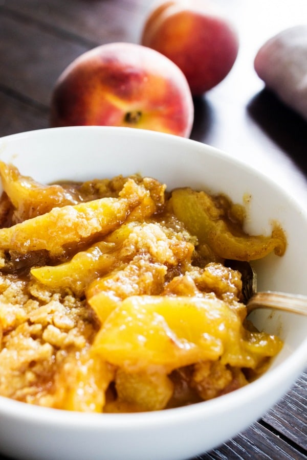 Best Ever Peach Cobbler Recipe - This classic & traditional dessert is made with just a few simple ingredients and is so easy to make. BEST EVER PEACH COBBLER RECIPE. White bowl, peaches, metal spoon, wooden table