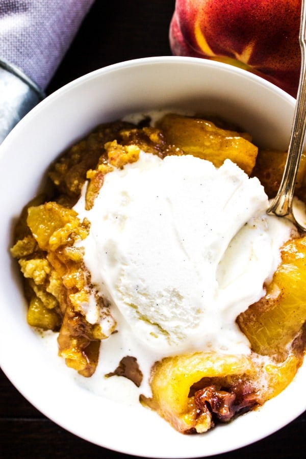 Best Ever Peach Cobbler Recipe - This classic & traditional dessert is made with just a few simple ingredients and is so easy to make. BEST EVER PEACH COBBLER RECIPE. White bowl, grey napkin, peaches, metal spoon