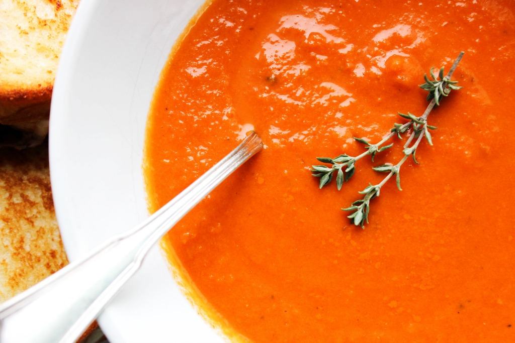 up close photo of tomato soup in a bowl with a sprig of thyme