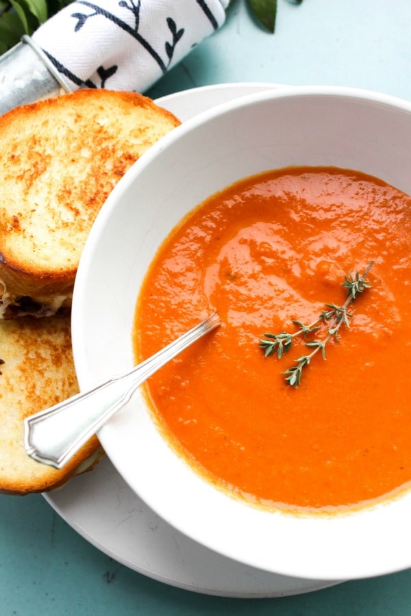 SLOW COOKER TOMATO SOUP -Metal spoon, white bowl and plate on blue table 