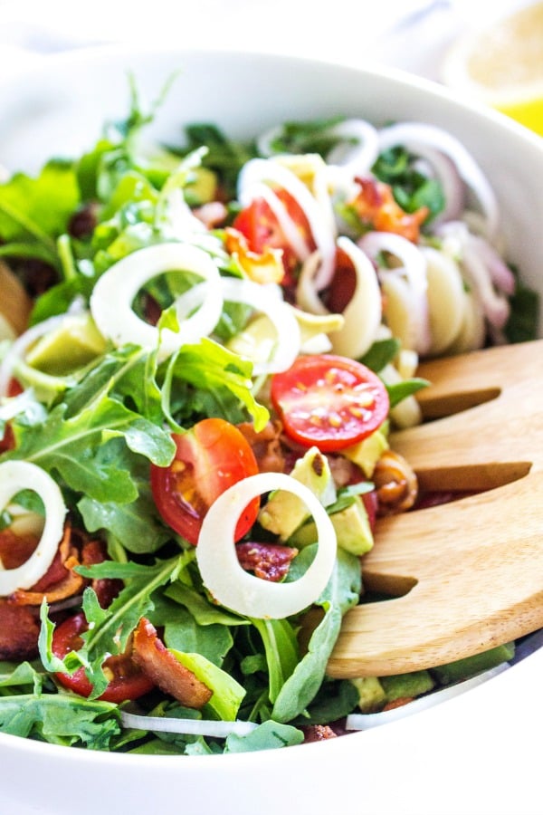 ARUGULA AND HEARTS OF PALM SALAD - this Brazilian inspired salad is rich with flavor and dressed in a light, sweet lemon vinaigrette. arugula and hearts of palm salad in a white bowl with wooden salad tong