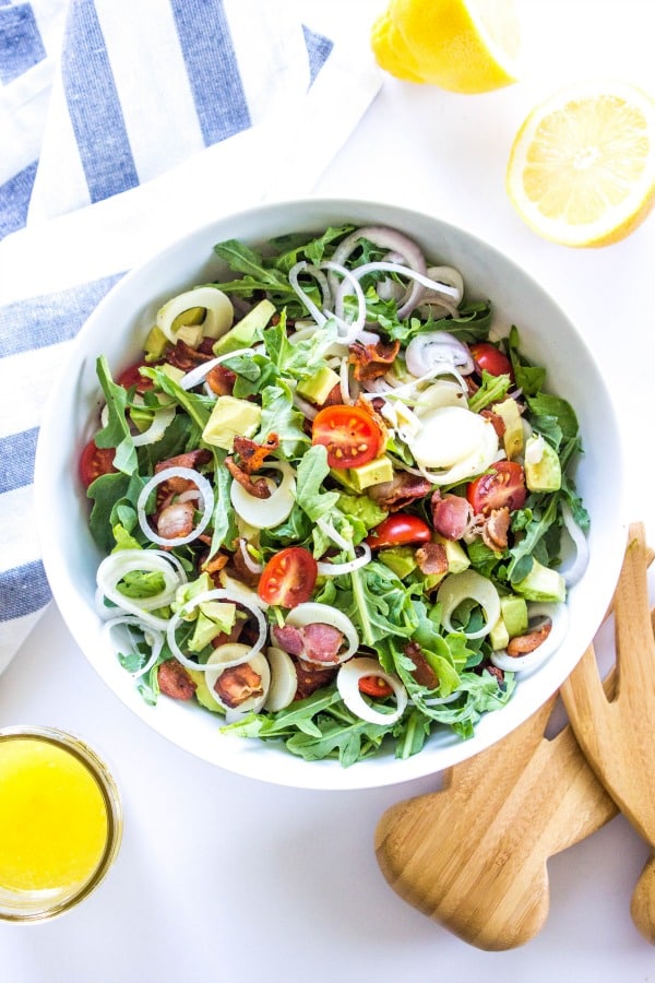 ARUGULA AND HEARTS OF PALM SALAD - this Brazilian inspired salad is rich with flavor and dressed in a light, sweet lemon vinaigrette. overhead white bowl with arugula salad and dressing