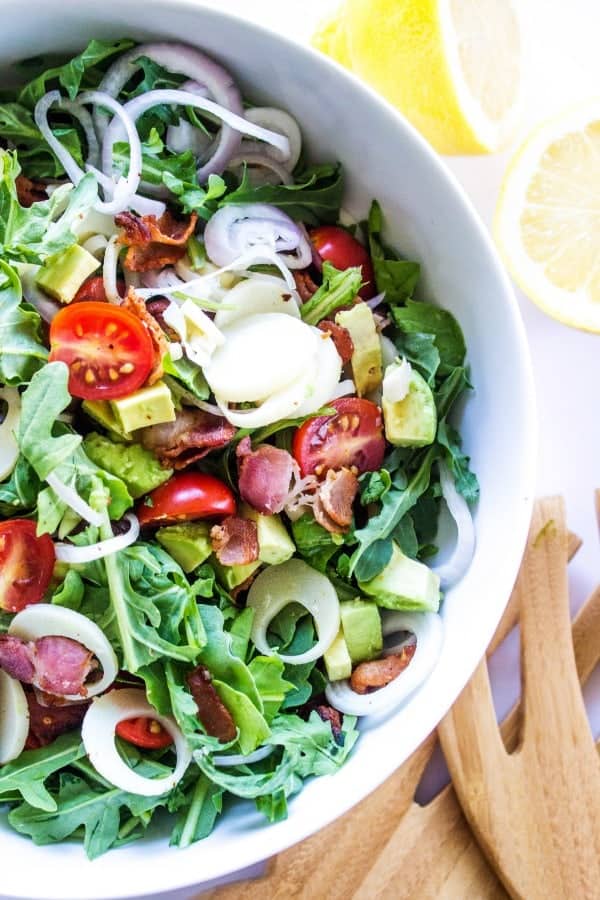 ARUGULA AND HEARTS OF PALM SALAD - this Brazilian inspired salad is rich with flavor and dressed in a light, sweet lemon vinaigrette. arugula salad white bowl with wooden salad spoons on side