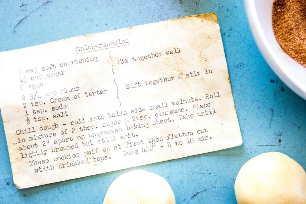 Original recipe card on blue tray with cinnamon and raw cookies dough