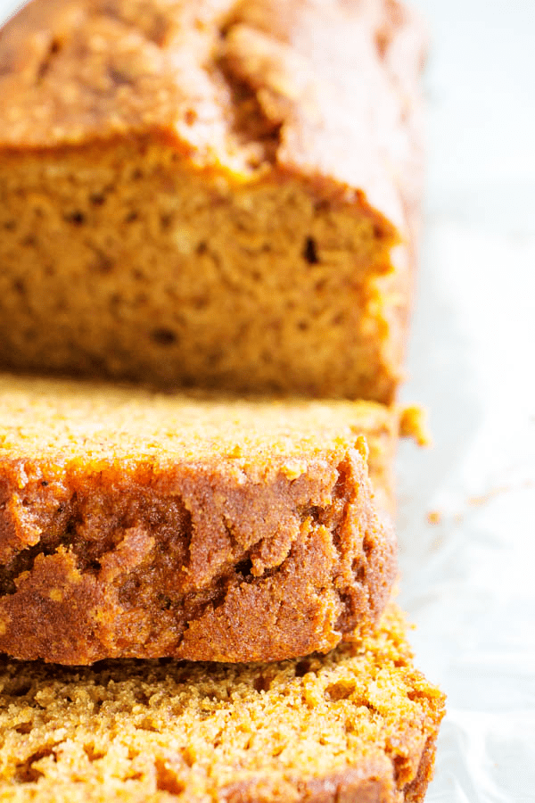 GLUTEN-FREE PUMPKIN BREAD - a quick bread that is deliciously spiced with nutmeg, cinnamon, & cloves. This fall treat is a family favorite. Close up of gluten-free pumpkin bread loaf with 2 pieces sliced