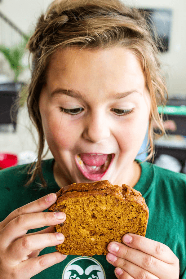GLUTEN-FREE PUMPKIN BREAD - a quick bread that is deliciously spiced with nutmeg, cinnamon, & cloves. This fall treat is a family favorite. Photo of girl about to bite into a slice of gluten-free pumpkin bread