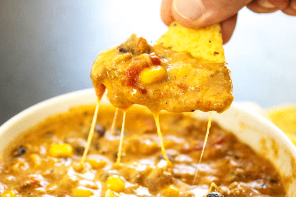 SLOW COOKER CHILI CHEESE DIP – cheesy and full of flavor, this easy recipe will score a win on game day and be a hit during the holidays. photo of tortilla chip dipped in slow cooker chili cheese dip with cheese pull