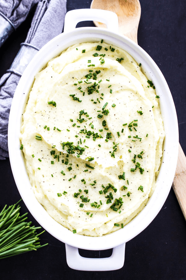 overhead shot mashed potatoes topped with chopped chives in white serving dish
