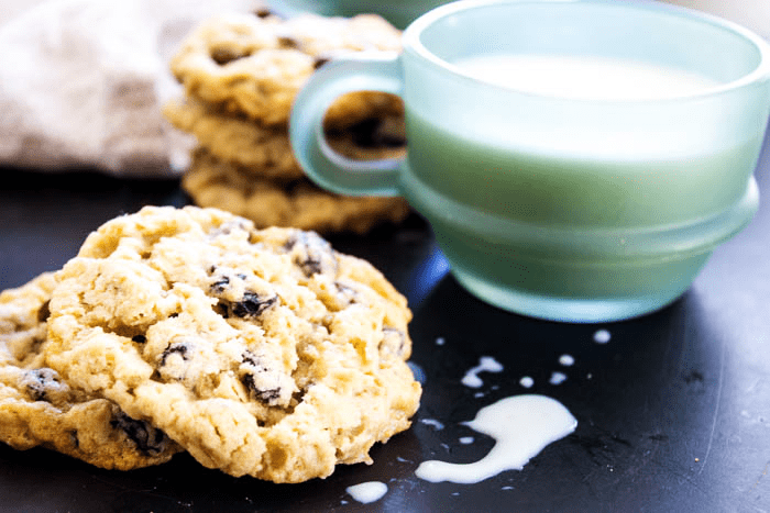 Oatmeal Raisin Cookies in stacks next to a glass mug of milk