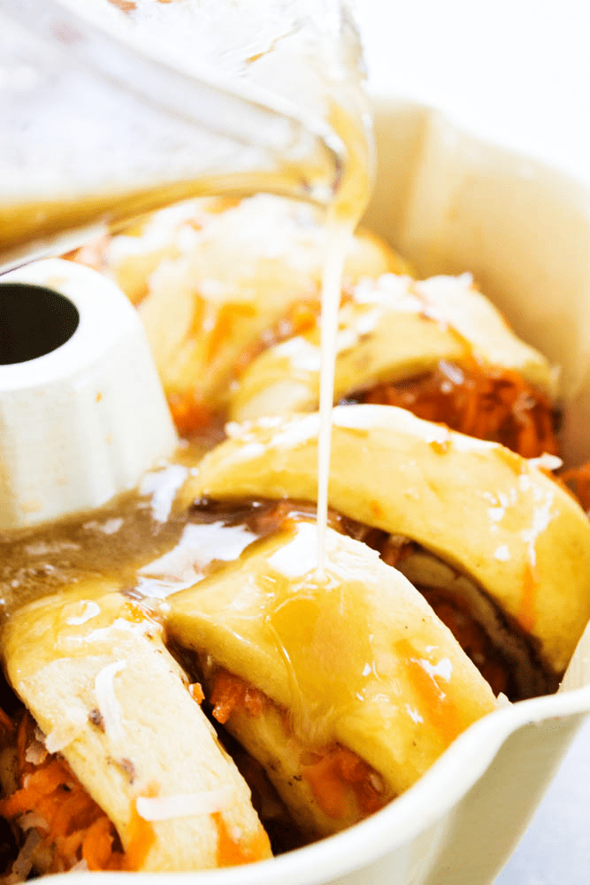 photo drizzling glaze over carrot cake monkey bread dough in pan