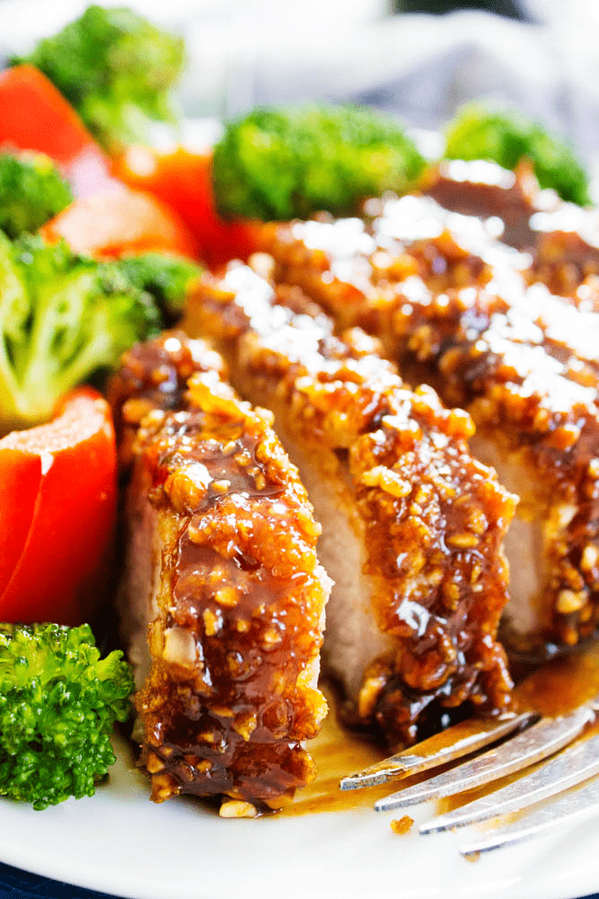 Cashew Oven-Fried Pork Chops sliced, served on a plate with broccoli and red peppers
