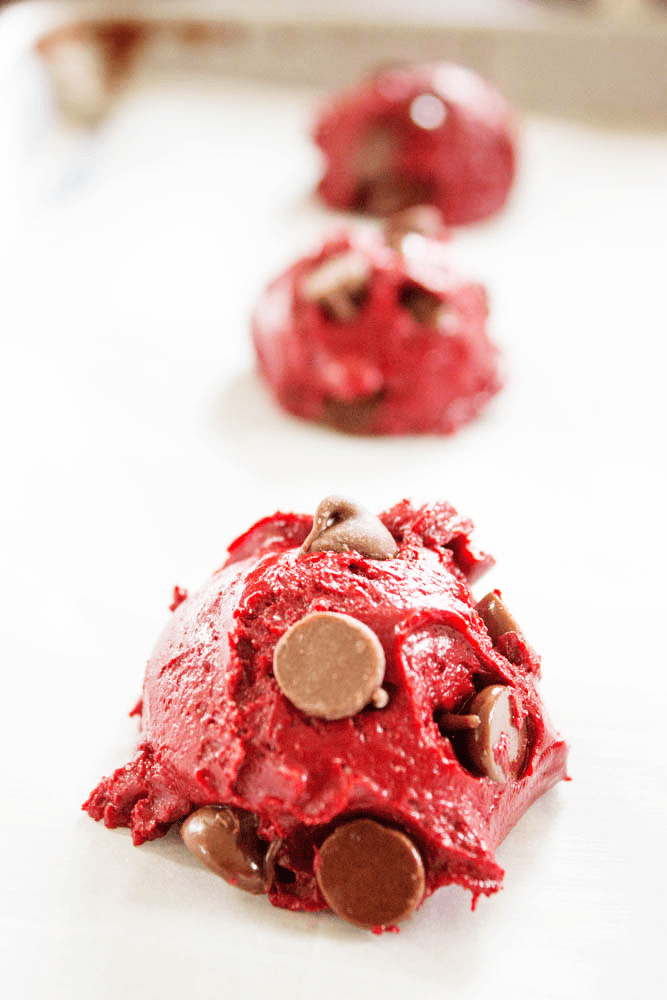 photo of balls of red velvet cookie dough on a parchment lined sheet pan