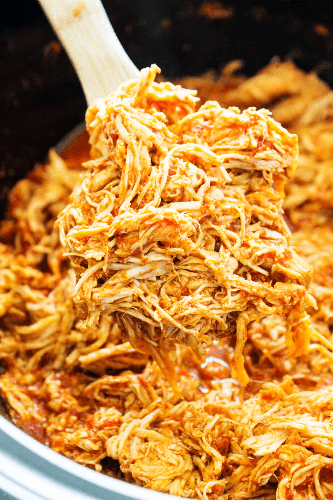 Chile Colorado Slow Cooker Chicken in the slow cooker with a wooden spoon