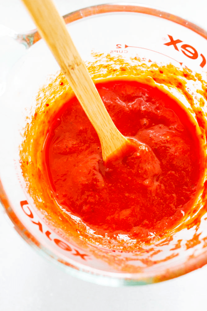 chile colorado sauce in a pyrex measuring cup with a small wooden stirring spoon