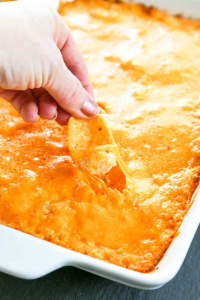 Buffalo Chicken Dip in baking dish, hand dipping in a fritos chip