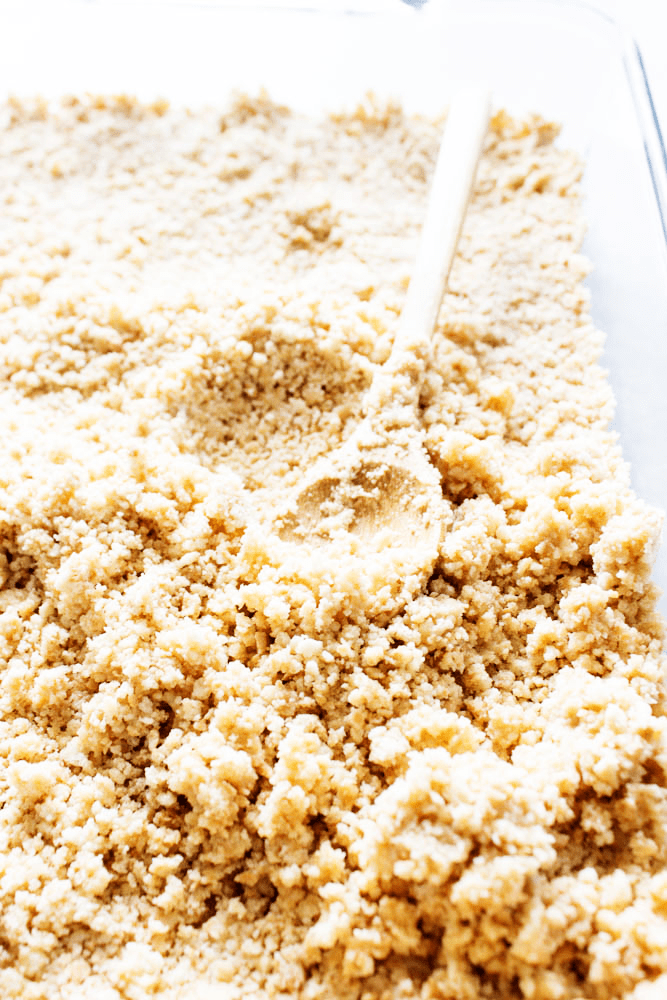 photo of crumb crust being pressed into a glass pan with a small spoon